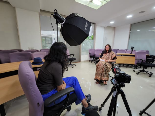 Two women in a recording studio setting with lights and cameras, conducting an interview in an office space.