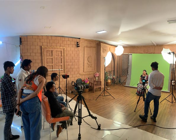 Film crew shooting a video in a studio with a green screen background.
